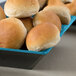 A blue square melamine bowl filled with bread rolls.
