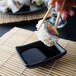 A person holding a sushi roll over a bowl of soy sauce with a pair of chopsticks.