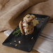 A GET black rectangular melamine platter with a cookie ice cream sandwich on it.