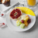 A white melamine plate with a bagel, fruit and a glass of orange juice on it.
