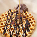 A waffle topped with chocolate syrup and nuts on a table.