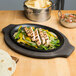 A Lodge cast iron fajita skillet with grilled chicken and vegetables on a wooden table.