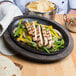A Lodge pre-seasoned cast iron fajita skillet with grilled chicken and vegetables on a table.