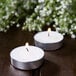 Two Leola white tea light candles burning on a table with flowers.