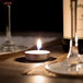 A Leola white tea light candle on a table with wine glasses and a bottle of wine.