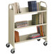 A Safco sand three-shelf book cart with books on it.
