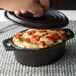 A person holding an American Metalcraft mini cast iron oval dutch oven filled with food.