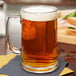 A Libbey glass mug of beer on a table with sandwiches.