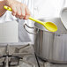 A person stirring a pot of soup with a yellow Vollrath high heat nylon prep spoon.
