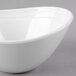 A white GET Magnolia melamine oval bowl with a textured rim on a gray surface.