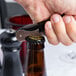 A hand opens a bottle of beer with a Franmara Duo-Lever Waiter's Corkscrew with a black enamel handle.