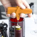 A hand using a Franmara Traveler's Orange plastic corkscrew and bottle opener to open a wine bottle.