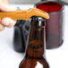 A hand using a yellow Franmara plastic bottle opener to open a brown bottle.