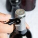 A hand using a Pulltap's Original Waiter's Corkscrew with a dark blue handle to open a bottle of wine.