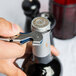 A hand using a Franmara Duo-Lever corkscrew with a navy blue enamel handle to open a bottle of wine.