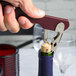 A hand using a Franmara Boomerang waiter's corkscrew to open a wine bottle.