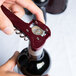 A person opening a bottle of wine with a Franmara Boomerang Waiter's Corkscrew with a burgundy handle.