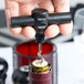 A hand holding a Franmara black plastic pocket corkscrew and opening a wine bottle.