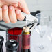 A hand using a Franmara curved stainless steel waiter's corkscrew to open a bottle of wine.