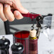 A hand using a Pulltap's Original Waiter's Corkscrew with a burgundy handle to open a wine bottle.