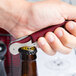 A hand with a Pulltap's Original customizable waiter's corkscrew with a burgundy handle opening a bottle.