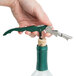A hand using a Franmara Duo-Lever Corkscrew with a green and black handle to open a bottle of wine.