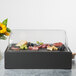 A Vollrath black food display platter in a glass case with food on a counter.