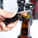 A hand using a Franmara two-lever waiter's corkscrew with a black handle to open a bottle of beer.
