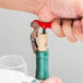 A person using a Franmara customizable waiter's corkscrew with a red enamel handle to open a cork in a wine bottle.