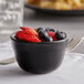 A Tuxton black china bouillon cup filled with blueberries on a table.
