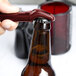 A hand using a red Franmara Traveler's corkscrew to open a brown beer bottle.