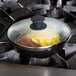 Lodge 8" tempered glass cover on a pan with bacon and eggs cooking on a stove.