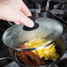 A person's hand using a Lodge tempered glass lid to cover a pan of cooking bacon.