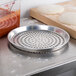 An American Metalcraft perforated aluminum pizza pan with dough on it.
