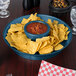 A blue HS Inc. polypropylene deli server filled with chips and salsa on a table.