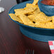 A blue polypropylene bowl filled with chips and salsa on a table.