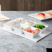 A rectangular white melamine platter with white bowls and a plate of sushi on a table.