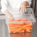 A person holding a Rubbermaid clear polycarbonate food storage container filled with carrots.