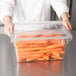 A person holding a Rubbermaid clear polycarbonate food storage box lid filled with carrots.