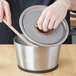 A hand holding a Vollrath stainless steel cover over a pot.