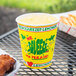 A yellow Squat "We Squeeze to Please" paper cup filled with lemonade on a table with fried chicken.
