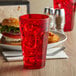 A close-up of a red GET plastic tumbler filled with red liquid and ice on a table with a burger.
