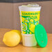 A 32 oz. Lemonade cup with a green lid on a counter filled with lemonade and ice.