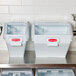 Two white Rubbermaid ingredient bins with sliding lids on a counter.