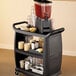 A black Carlisle utility cart with a beverage dispenser and cups on top.