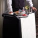 A man in a suit standing behind a Carlisle black utility cart with breakfast items on it.