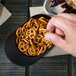 A person holding a bowl of pretzels made from a black mini baseball helmet.