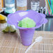 A purple flower-shaped sno-cone cup with a green slushy inside.