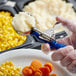 A person in gloves using a Vollrath blue and silver thumb press to scoop mashed potatoes.