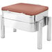A square stainless steel chafer with a copper lid on a metal stand with a brown cushion.